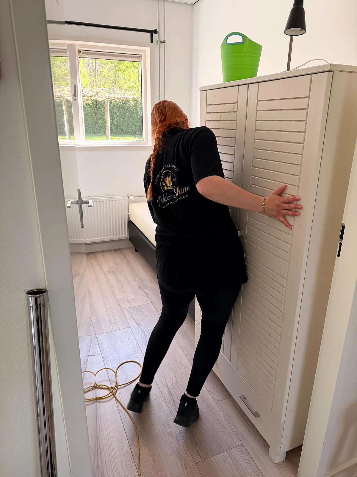 Medewerker van PolderShine verplaatst een kast tijdens de schoonmaak, met het logo zichtbaar op de werkkleding