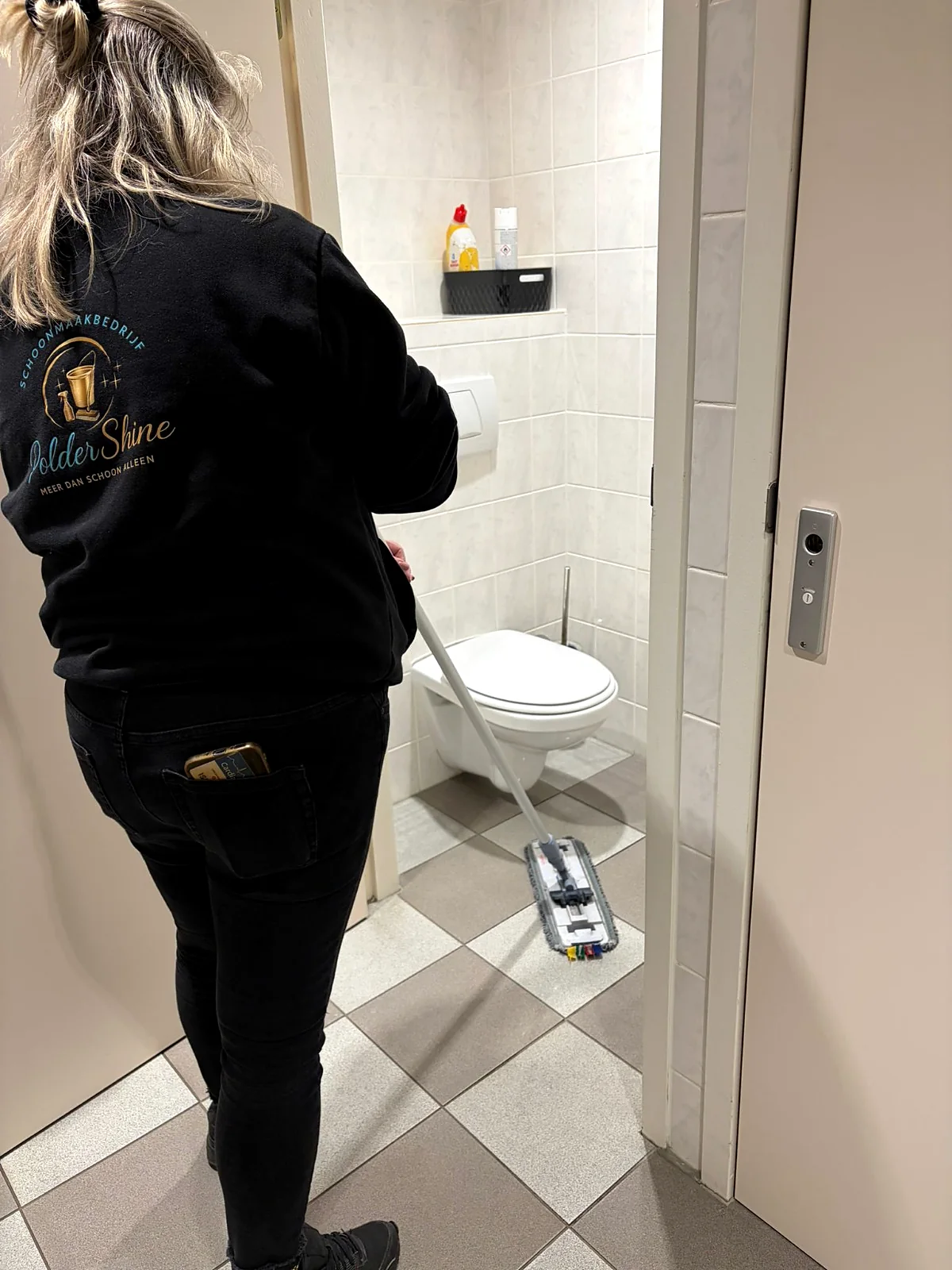 Medewerker van PolderShine maakt een toiletruimte schoon met een mop